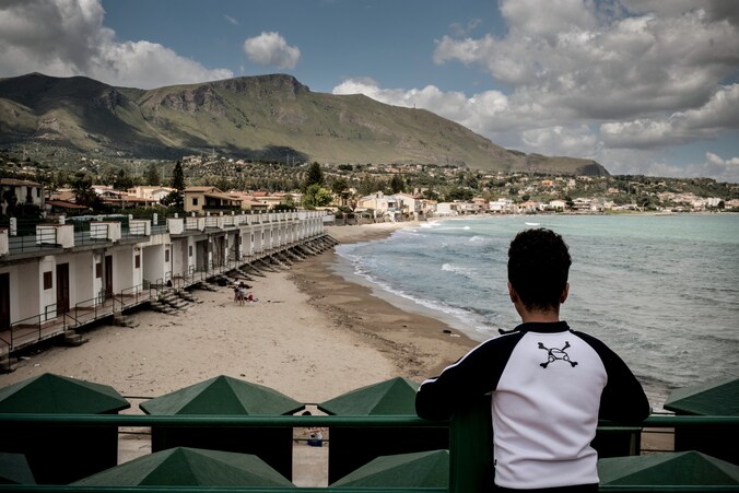 Een jongen die alleen naar Italië is gereisd kijkt uit over het strand van Sicilië.