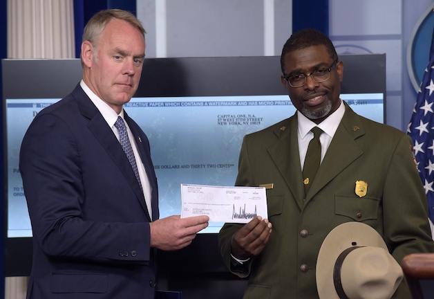Secretaris Ryan Zinke geeft de cheque aan Tyrone Brandyburg van de National Parks Service.