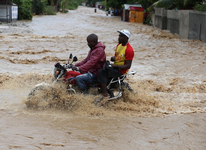 Mannen op een motorfiets steken een overstroomde straat over in Grand Goave.
