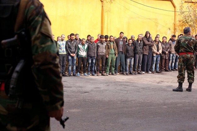 De militaire politie bewaakt mannen die uit de oostelijke wijken van Aleppo werden geëvacueerd en worden ingelijfd voor militaire dienst.
