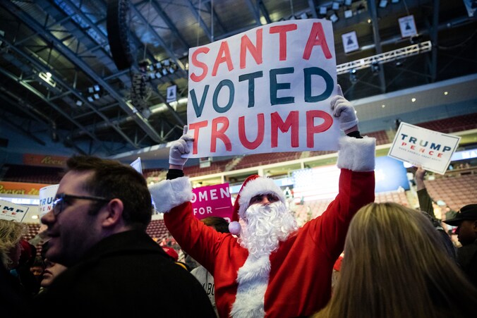 Een man met een kerstmanpak houdt een bord omhoog waarop staat dat 'de Kerstman voor Trump heeft gestemd'.