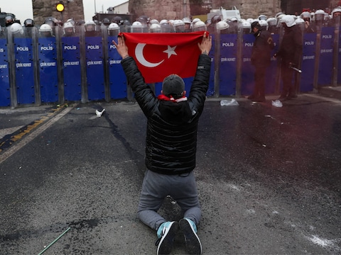 Een betoger knielt voor de politie met een Turkse vlag tijdens een protest tegen de arrestatie van Ekrem Imamoglu.