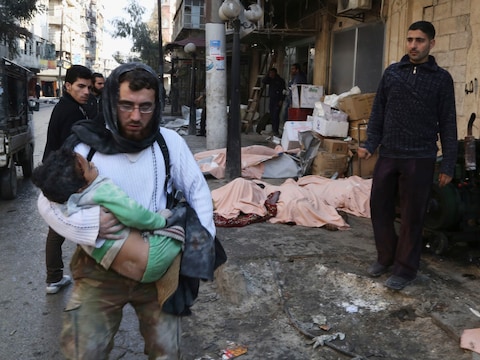 Een man draagt een gewond kind dat net onder het puin vandaan is gehaald na een bombardement in Aleppo.