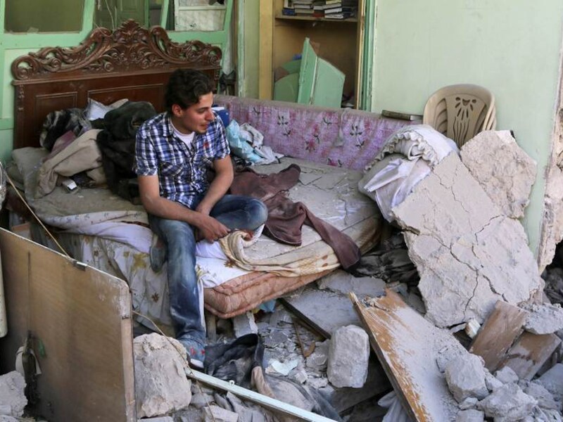 Een Syrische man in de puinhopen vam een slaapkamer nadat een vatenbom op het huis is gevallen.