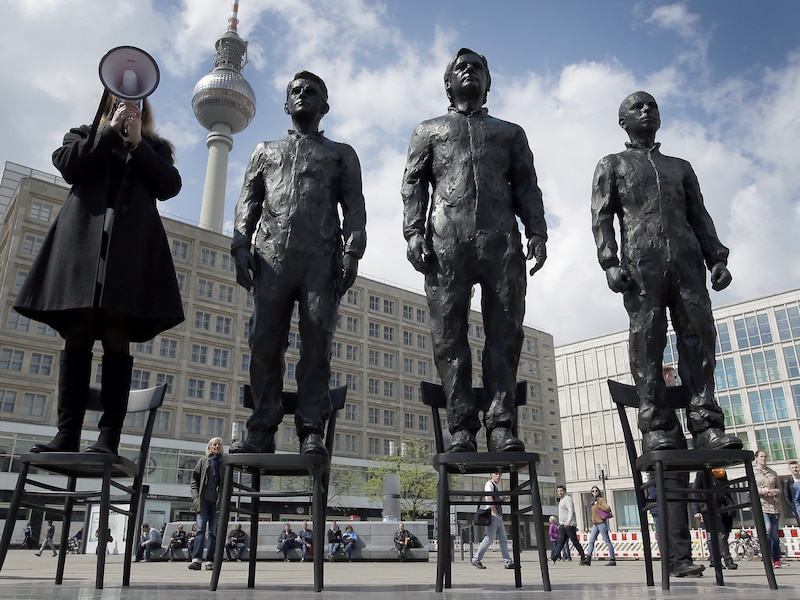 Een vrouw geeft een speech naast de levensgrote standbeelden van Snowden, Assange en Manning.