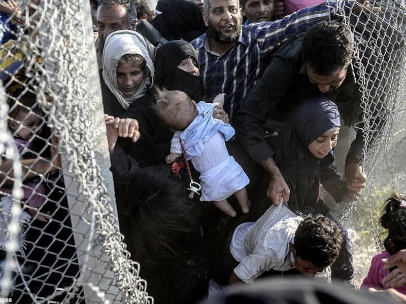 Door een gat in het metalen hek weten Syrische vluchtelingen Turkije te bereiken.