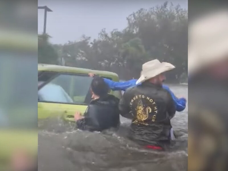 Op de beelden is te zien hoe een groep mannen – die tot hun middel in het water staan – de oudere man van zijn ondergelopen auto wegdragen. 
