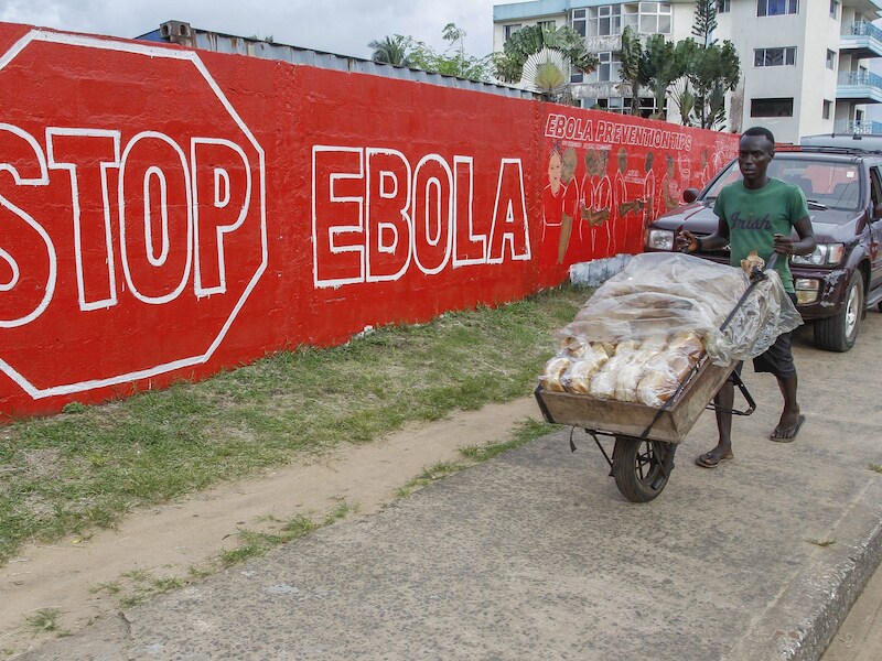 Een man uit Liberia duwt zijn broodkar langsheen een sensibiliseringscampagne ter bestrijding van het dodelijke Ebola-virus.